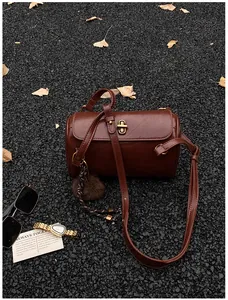 Détail d'un sac polochon marron avec fermoir doré sur fond de feuilles de ginkgo