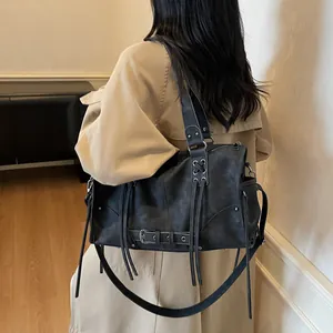 Borsa a tracolla moto retrò con borchie e nappe indossata da una modella in grigio