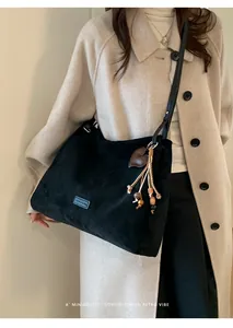 Chic black faux suede tote bag with heart tassel detail styled on a beige trench coat