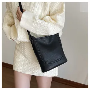 Détail d'un sac seau noir en cuir grainé porté par un mannequin en tenue décontractée