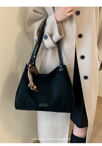 Detail of black faux suede tote bag with heart charm and leather strap on model