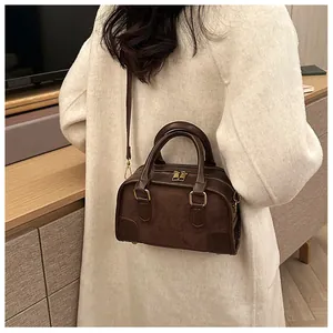 Détail d'un sac Boston marron foncé avec chaîne porté sur un manteau en laine blanc