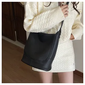 Détail du sac bandoulière noir en cuir grainé porté par un mannequin en robe