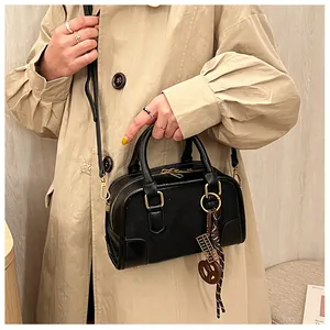 Détail du sac Boston noir en cuir grainé avec finitions dorées et pendentif décoratif
