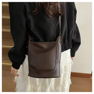 Détail du sac seau marron foncé à texture litchi avec surpiqûres en U et bandoulière