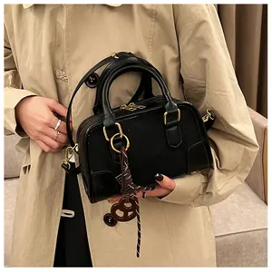 Détail du sac Boston en cuir noir avec ferrures dorées et breloque tressée marron