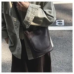 Gros plan sur le cuir grainé marron foncé et les coutures en U du sac à bandoulière