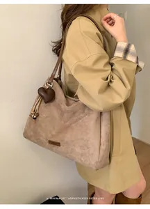 Detail view of khaki faux suede tote bag with heart charm and decorative fringe accent