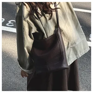 Vue de rue d'un sac seau bandoulière en cuir marron foncé avec une texture grainée de litchi
