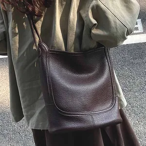 Sac bandoulière en cuir grainé marron avec surpiqûres en U porté par un mannequin