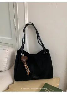 Detail of black faux suede tote bag featuring a heart charm with woven tassels and beads