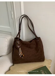 Detail of suede tote bag in dark brown with heart tassel charm and leather label