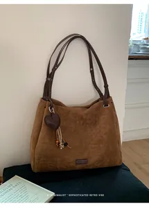 Close-up of retro brown suede tote bag featuring heart pendant and tassel details