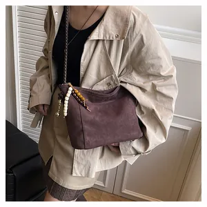 Détail du sac bandoulière en suède avec bandoulière tressée et pendentif à perles