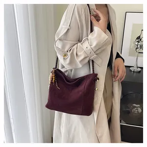 Détail d'un sac hobo en daim bordeaux avec pompon perlé porté par un mannequin