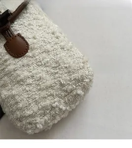 Close-up of soft bouclé fabric texture and brown leather strap detail on a crossbody bag