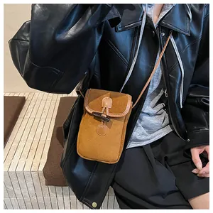 Detail of a vintage caramel suede crossbody phone bag with horn buckle on model