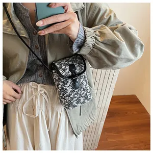Detail of tweed crossbody phone bag with black leather trim and round buckle on a model