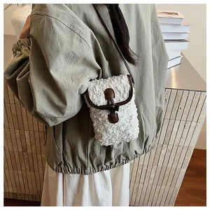 Detail of white plush crossbody bag featuring brown leather trim and horn button closure