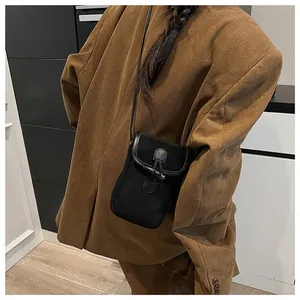 Close-up of a black canvas crossbody bag with leather trim on a brown corduroy jacket