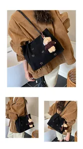 Detail of black faux suede hobo bag with cutout flowers and a cute plush bear charm
