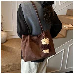Detail of dark brown suede tote bag with laser-cut flower patterns and bear charm