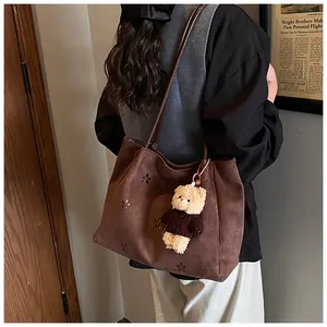 Macro view of vintage brown suede tote bag with laser-cut floral patterns and plush bear charm