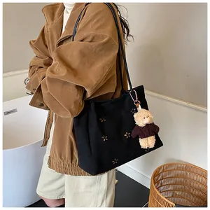 Detail of black canvas tote bag with floral patterns and a cute bear keychain accessory