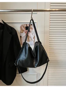 Detalle de un bolso hobo grande negro colgado en una pared blanca con decorado minimalista