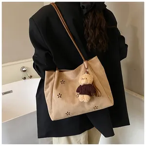 Detail of suede tote bag with flower cutouts and plush bear charm on model shoulder