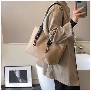 Dettaglio borsa tote in pelle scamosciata kaki con tracolla nera e nappe di legno