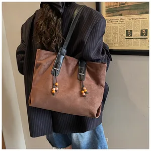 Dettaglio della borsa tote in pelle scamosciata marrone con ciondoli in legno e tracolla nera