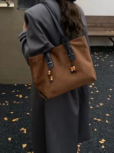 Dettaglio della borsa tote marrone scuro con ciondoli decorativi e trama scamosciata