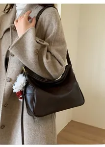 Détail du sac à bandoulière en cuir marron foncé avec coutures blanches et charme