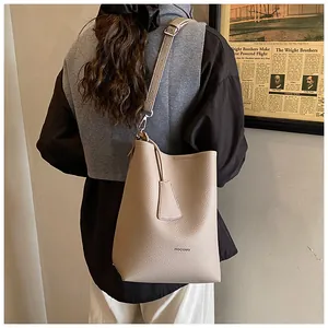 Détail du sac seau beige en cuir à motif litchi avec logo HOCOMU et bandoulière