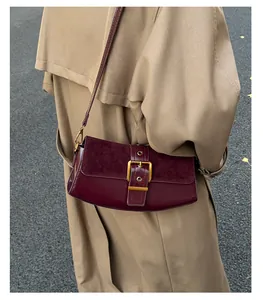 Detail of burgundy leather baguette bag with a large gold buckle on a beige trench coat