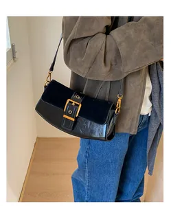 Detailed view of a black leather underarm bag with gold buckle on a stylish model