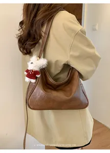 Détail du sac hobo en cuir marron vintage avec pendentif en peluche et logo embossé