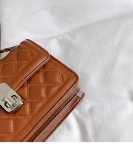 Detail einer braunen Steppledertasche mit silbernem Drehverschluss und Kettenriemen