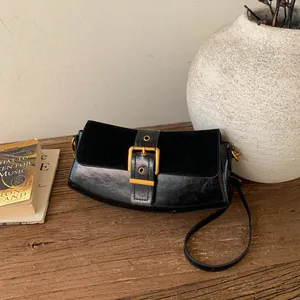 Vintage black underarm bag with suede flap and gold buckle on a rustic wooden table