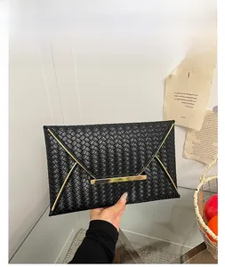 Détail d'une pochette enveloppe noire en cuir tressé avec fermoir métallique doré