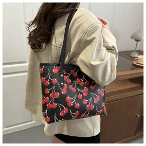 Détail d'un sac cabas noir à imprimé cerise avec lettrage doré et fines lanières