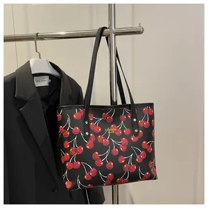 Détail du cabas à imprimé cerise avec logo doré suspendu à côté d'un blazer noir