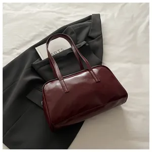 Detail view of wine red glossy leather shoulder bag placed on a grey blazer with a book