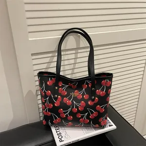 Sac fourre-tout noir avec imprimé cerise et logo doré sur un fond texturé élégant