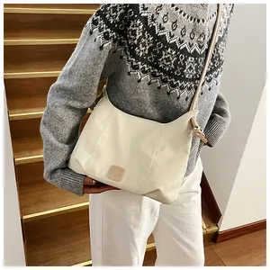 Sac hobo blanc cassé chic avec écusson carré porté par un mannequin élégant