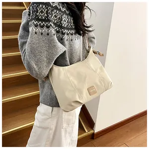 Détail d'un sac hobo en cuir beige avec un écusson carré Fashion situé au centre du sac