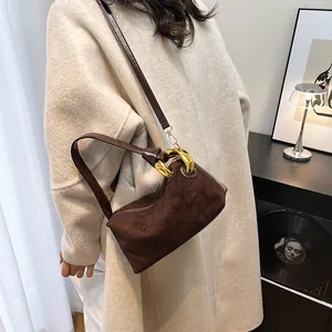 Brown suede baguette bag with gold chain strap shown on model in minimal interior
