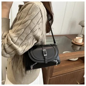 Gros plan d'un sac porté épaule noir en similicuir avec fermetures éclair sur un pull beige