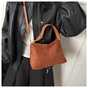 Close-up of brown suede crossbody bag with adjustable strap on black leather jacket